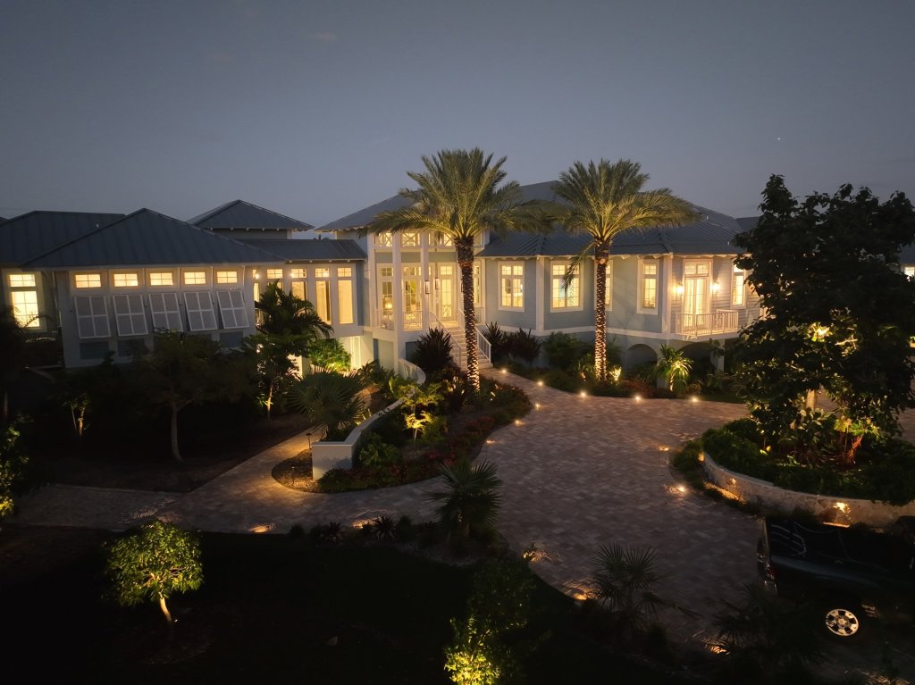 Casa inteligente en la playa con palmas y jardín iluminados al anochecer con luminarias exteriores de grado costero