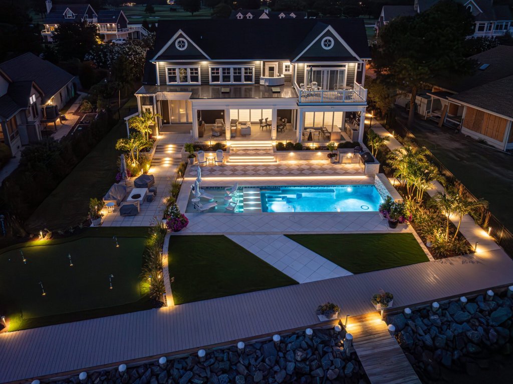 Villa de lujo frente al agua de noche con piscina, terrazas e iluminación exterior automatizada para alquiler premium