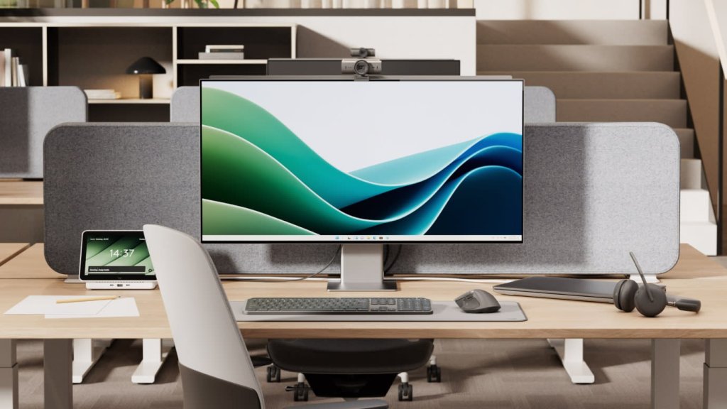 Oficina en casa con monitor, cámara web sobre la pantalla, audífonos con micrófono y teclado inalámbrico